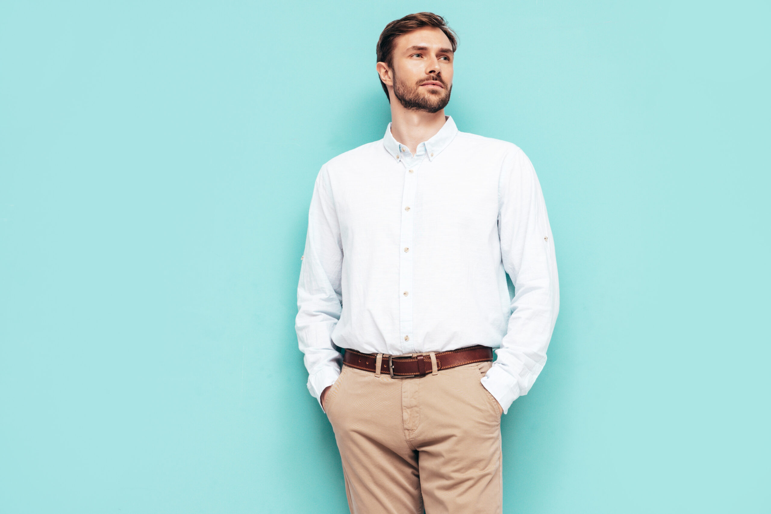 Portrait of handsome smiling model. Sexy stylish man dressed in shirt and trousers. Fashion hipster male posing near blue wall in studio. Isolated